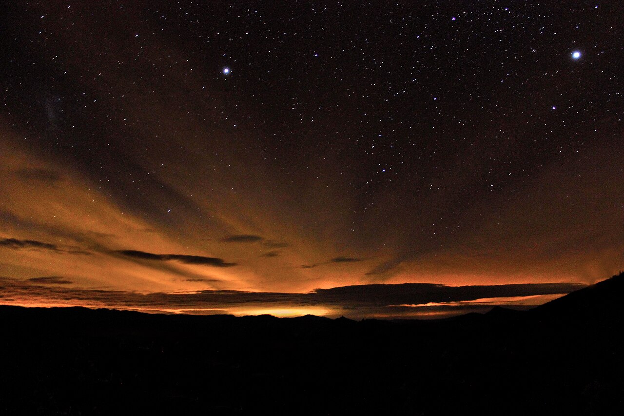 Céu estrelado e faixa alaranjada sobre as montanhas à noite em Delfim Moreira, Minas Gerais.